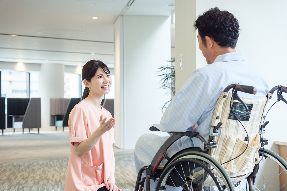 車椅子に乗った患者と会話をする看護師